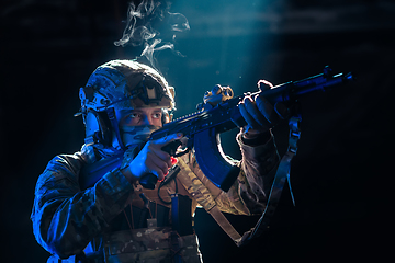 Image showing Army soldier in Combat Uniforms with an assault rifle and combat helmet night mission dark background. Blue and purple gel light effect.