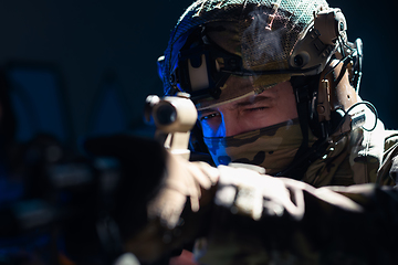 Image showing Army soldier in Combat Uniforms with an assault rifle and combat helmet night mission dark background. Blue and purple gel light effect.