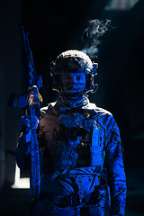 Image showing Army soldier in Combat Uniforms with an assault rifle and combat helmet night mission dark background. Blue and purple gel light effect.