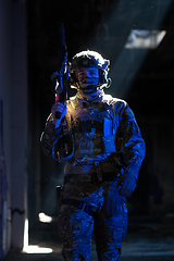 Image showing Army soldier in Combat Uniforms with an assault rifle and combat helmet night mission dark background. Blue and purple gel light effect.