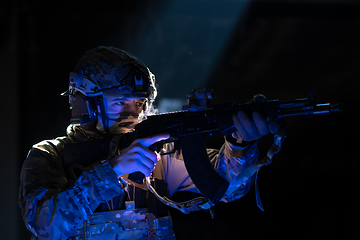 Image showing Army soldier in Combat Uniforms with an assault rifle and combat helmet night mission dark background. Blue and purple gel light effect.