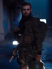 Image showing Army soldier in Combat Uniforms with an assault rifle and combat helmet night mission dark background. Blue and purple gel light effect.