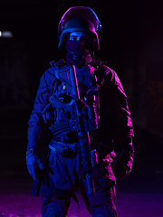 Image showing Army soldier in Combat Uniforms with an assault rifle and combat helmet night mission dark background. Blue and purple gel light effect.