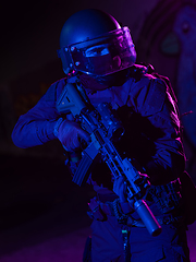 Image showing Army soldier in Combat Uniforms with an assault rifle and combat helmet night mission dark background. Blue and purple gel light effect.