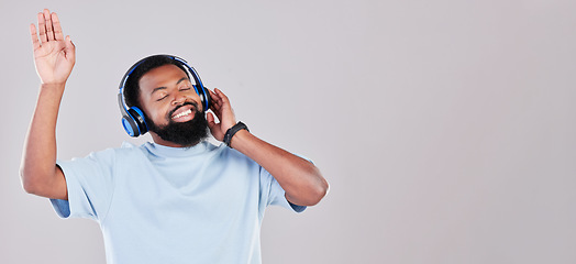 Image showing Headphones, happy and young man in a studio listening to music, playlist or album while dancing. Happiness, smile and African male model streaming song or radio by gray background with mock up space.