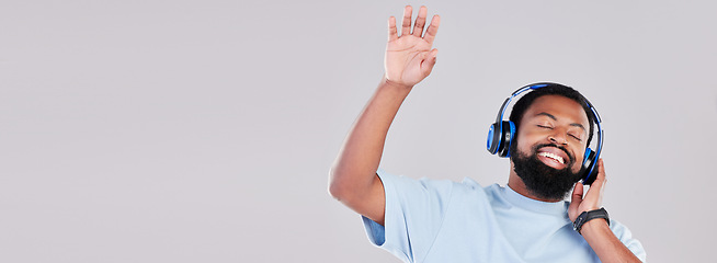 Image showing Headphones, mockup and young man in a studio listening to music, playlist or album while dancing. Happy, smile and African male model streaming a song or radio by a gray background with mock up space