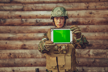 Image showing Woman soldier using tablet computer against old wooden wall in camp