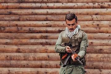 Image showing A soldier in uniform with a rifle in his hand is standing in front of a wooden wall. A soldier guards the forest base from the enemy