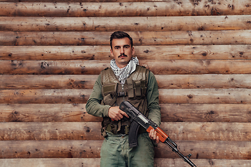 Image showing A soldier in uniform with a rifle in his hand is standing in front of a wooden wall. A soldier guards the forest base from the enemy