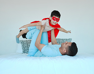 Image showing Bonding, bedroom and father playing with his child for quality time, fun or happiness at home. Happy, smile and young dad relaxing with his boy kid in a superhero costume on the bed at family house.