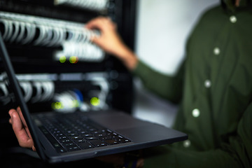 Image showing Server room maintenance, laptop and technician at work for cyber security and building network. Programming, coding and a person or it worker with a computer for a connection system in the workplace