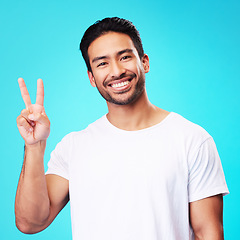 Image showing Portrait, man and peace fingers in studio for hope, self love and show icon on blue background. Face of happy asian male model, v sign and hands for victory, good mood and emoji in support of freedom