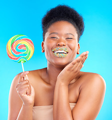 Image showing Candy, portrait and woman with sprinkles on her lips in a studio with sweet treats, dessert or snack. Happy, smile and young African female model with a colorful lollipop isolated by blue background.