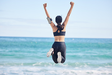 Image showing Happy woman, fitness and jump in achievement on beach for winning, workout success or outdoor exercise. Rear view of excited female person in celebration for accomplishment or training by the ocean