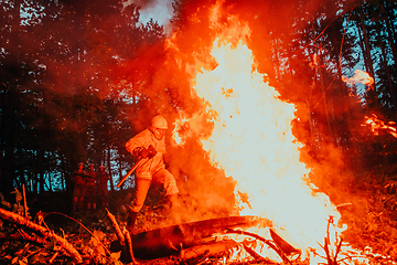 Image showing firefighter hero in action danger jumping over fire flame to rescue and save