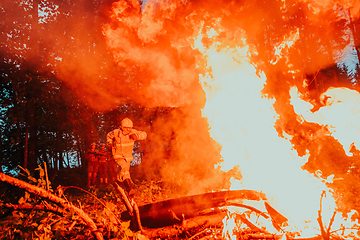 Image showing firefighter hero in action danger jumping over fire flame to rescue and save