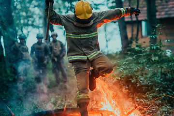 Image showing firefighter hero in action danger jumping over fire flame to rescue and save