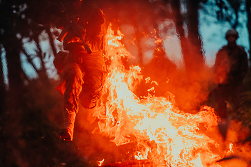 Image showing Soldier in Action at Night in the Forest Area. Night Time Military Mission jumping over fire