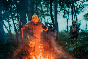 Image showing firefighter hero in action danger jumping over fire flame to rescue and save