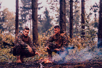 Image showing Two exhausted soldiers sitting by the fire after a weary and heavy war battle