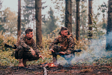 Image showing Two exhausted soldiers sitting by the fire after a weary and heavy war battle