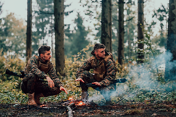 Image showing Two exhausted soldiers sitting by the fire after a weary and heavy war battle