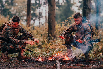 Image showing Two exhausted soldiers sitting by the fire after a weary and heavy war battle