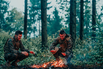 Image showing Two exhausted soldiers sitting by the fire after a weary and heavy war battle