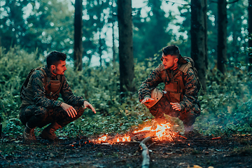 Image showing Two exhausted soldiers sitting by the fire after a weary and heavy war battle