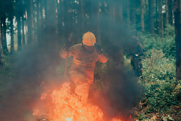 Image showing firefighter hero in action danger jumping over fire flame to rescue and save