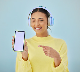 Image showing Happy woman, phone mockup and pointing for advertising or marketing against a studio background. Female person smile and listening to music on headphones with mobile smartphone app display or screen