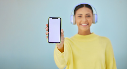 Image showing Happy woman with phone screen, headphones and mockup in studio for social media post, mobile app and streaming radio. Smile, music media subscription and girl with cellphone on blue background space.