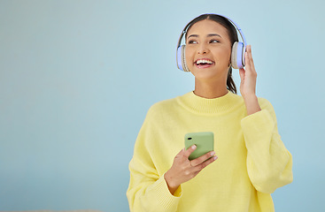 Image showing Happy woman with phone, headphones and banner mockup in studio on social media, mobile app and streaming radio. Smile, relax and music media subscription, girl with cellphone on blue background space