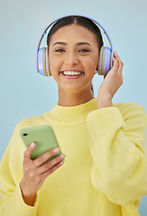 Image showing Portrait of woman with phone, headphones and smile in studio for social media, mobile app and streaming radio site. Podcast, music media subscription and happy girl with cellphone on blue background.