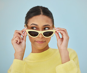 Image showing Sunglasses, gen z and young woman in a studio with a casual, stylish and cool sweater outfit. Confident, face and female model with trendy style and fashion accessory isolated by a blue background.