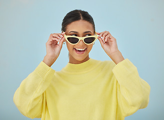 Image showing Happy, sunglasses and young woman in a studio with a casual, stylish and cool sweater outfit. Happiness, smile and female model with trendy style and fashion accessory isolated by a blue background.