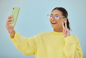 Image showing Selfie, peace sign and happy studio woman with emoji v sign, icon and pose for social network, memory picture or photography. Gen z person, youth or influencer post to media app on blue background