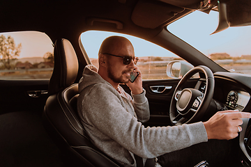 Image showing A man with a sunglasses driving a car and talking on smartphone at sunset. The concept of car travel