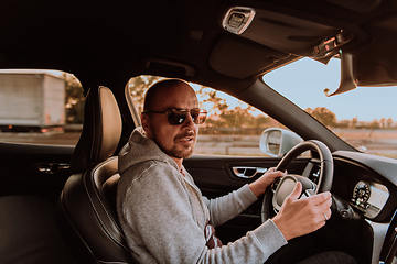 Image showing A man with a sunglasses driving a car at sunset. The concept of car travel