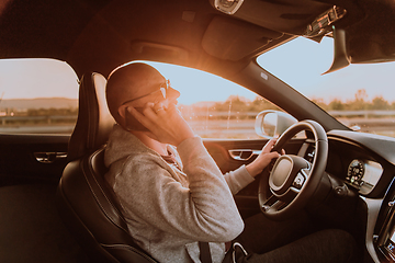 Image showing A man with a sunglasses driving a car and talking on smartphone at sunset. The concept of car travel