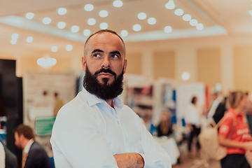 Image showing Portrait of a business man with a beard. In the background, a group of business people preparing for the start of the conference