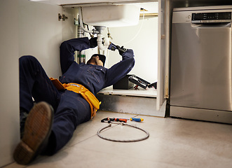 Image showing Kitchen, maintenance and renovation with a plumber on the floor of a home to fix a leak, issue or problem. Plumbing, repair and tools with a handyman or contractor working on a pipeline in a house