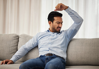 Image showing Armpit stink, smelling and a man on the sofa with a hygiene or bacteria problem. Bad, home and an Asian person with body odor, underarm sweat or grooming issue on the living room couch after work