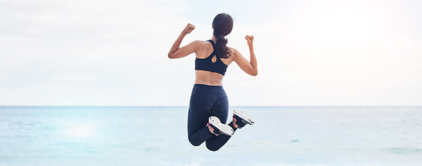 Image showing Back, freedom and fitness woman jump at the beach with celebration after running, training or workout success in nature. Exercise, jumping and behind female at the sea celebrating goal milestone
