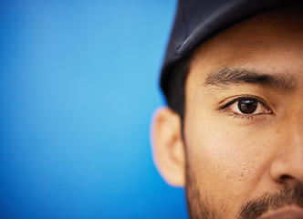 Image showing Eye, closeup and portrait of half of man in sports on blue background with advertising, mockup or space with athlete in studio. Serious, face and Indian person in cricket or baseball cap and fitness