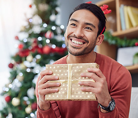 Image showing Christmas, smile and asian man with gift in his home happy, excited and having fun holiday celebration. Hand holding, box and Japanese male with present in a living room at December party or event