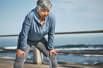 Image showing Senior, exercise and tired woman at the beach on break from training, workout or morning cardio run in nature. Sports, fatigue and elderly female runner stop to breathe on ocean workout or fitness