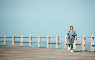 Image showing Fitness, running and senior woman at the beach for exercise, health or cardio on blue sky background. Training, wellness and elderly female runner at the sea for morning workout, routine or ocean run