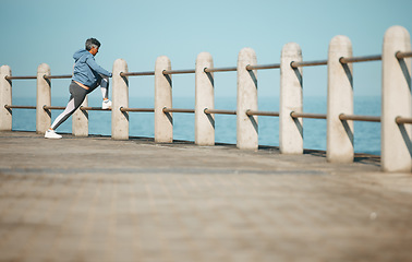 Image showing Senior, fitness and woman at the beach stretching for exercise, health and morning cardio routine. Leg, stretch and elderly female runner at the sea for training, wellness and flexible for ocean run