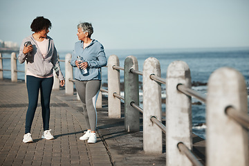 Image showing Fitness, walking and women by ocean talking for healthy lifestyle, wellness and cardio on promenade. Sports, friends and female people in conversation on boardwalk for exercise, training and workout